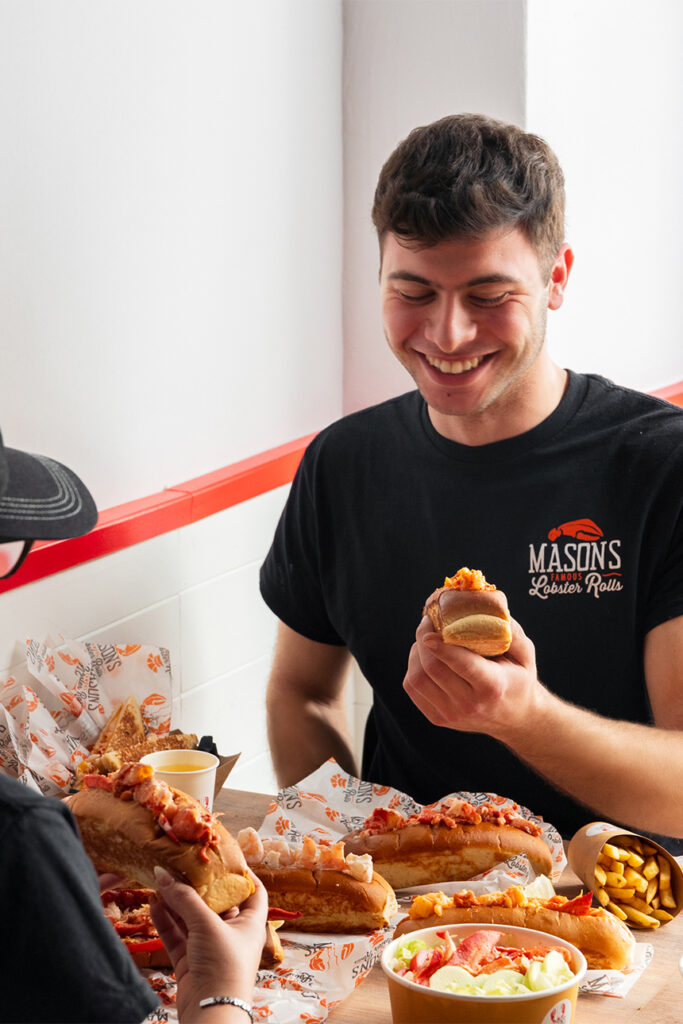 Amici condividono lobster roll Mason's, coleslaw e patatine seduti allo stesso tavolo