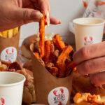 Mano che prende una patatina di patata dolce accanto a un lobster roll Mason's