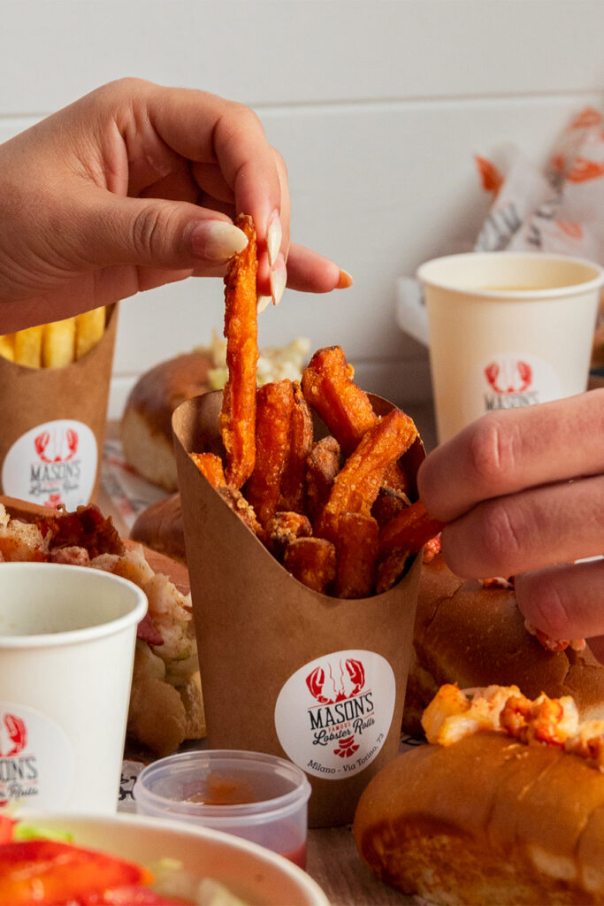 Mano che prende una patatina di patata dolce accanto a un lobster roll Mason's